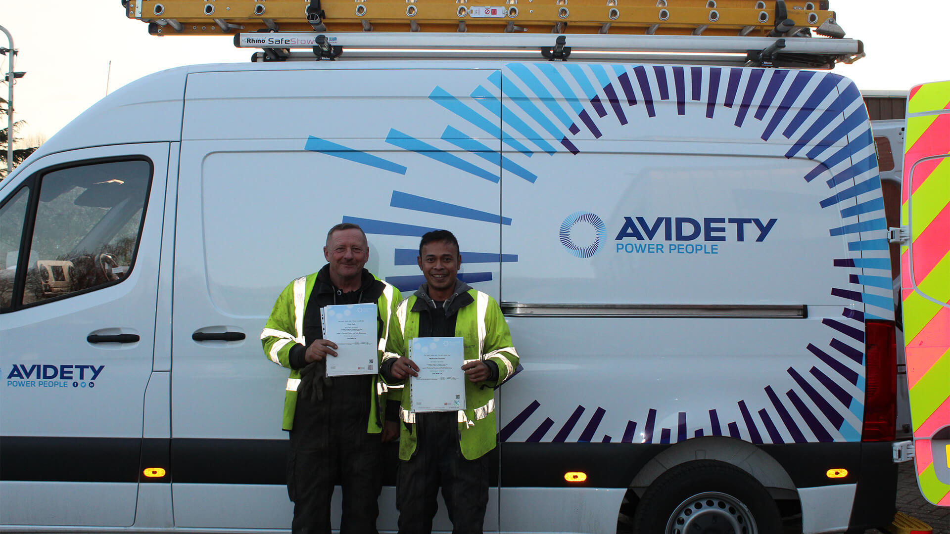 2 Men Standing in Front of Avidety Van in High Visibility Jackets, Holding Certificates
